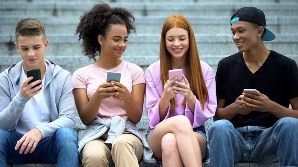 Happy multiethnic friends scrolling social networks app by smartphones outdoor - Fotó, kép