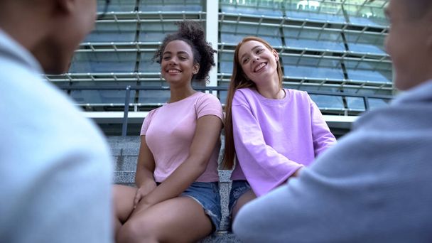 Young female students looking at male classmates, friends spending time outdoors - Photo, Image
