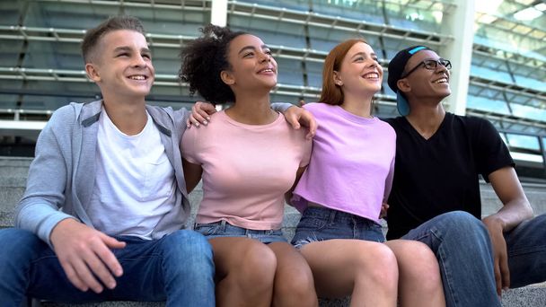Cheerful teenage friends hugging sitting stadium together, multiracial students - Foto, immagini