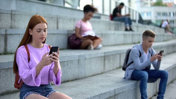 College students chatting by smartphones, teenagers scrolling social network app - 写真・画像