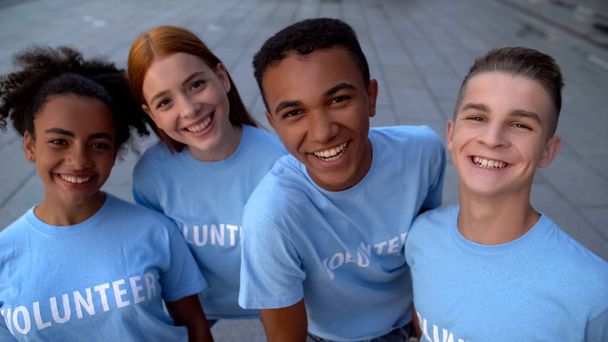 Glad college students in volunteer t-shirts looking camera, support togetherness - 写真・画像