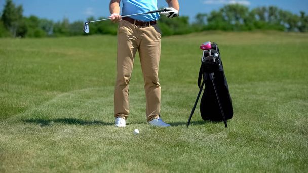 Golf coach holding iron club, preparing to hit ball, sport equipment bag nearby - Fotó, kép