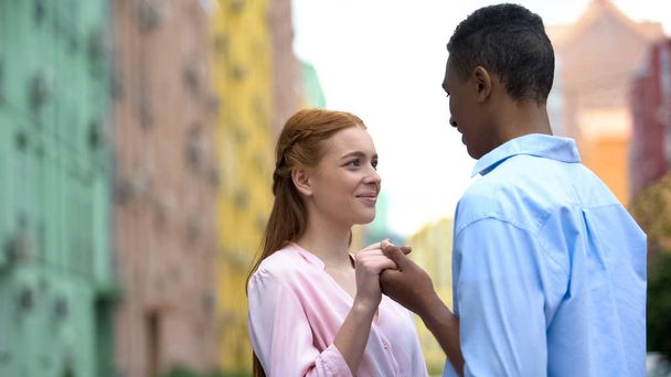 Pretty couple holding hands and looking at each other against colorful buildings - Photo, Image