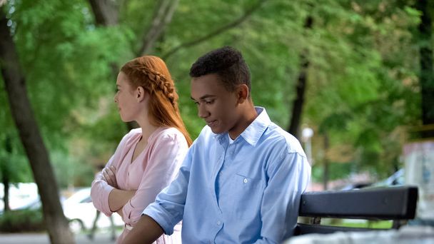 Offended teen girlfriend and boyfriend sitting separately on bench in park - Foto, imagen