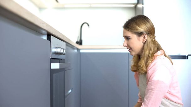 Young woman looking at oven, planning dishes for family dinner, housework - Foto, Imagem