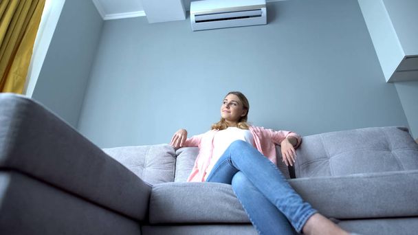 Girl cooling down on hot day sitting on couch under air conditioner, bottom view - Photo, Image
