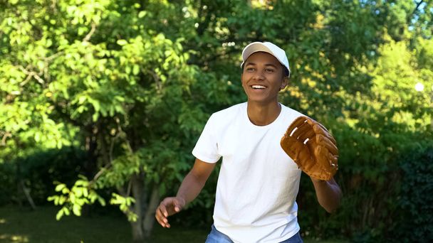 Glad teen boy in white cap smiling after baseball shot, favorite hobby, sport - Foto, afbeelding