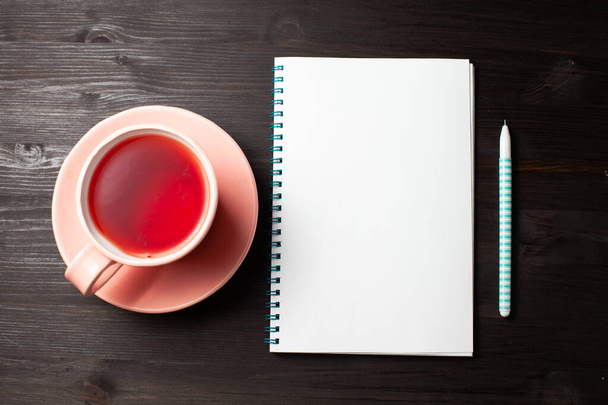 Open notebook, cup of tea, pen on black background - Foto, afbeelding