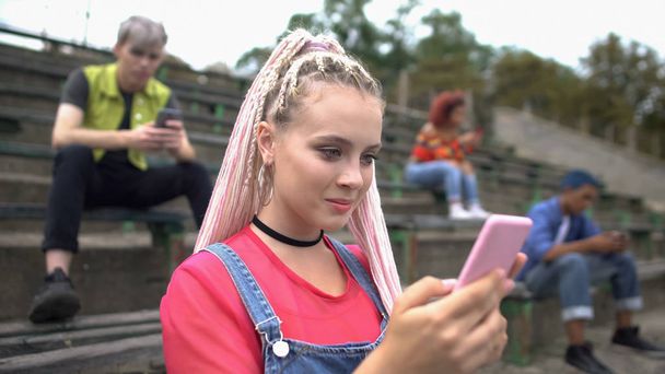 Excited pretty teenager reading smartphone message sitting stadium stairs, news - 写真・画像