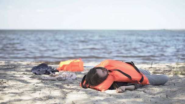 Young woman in life jacket lying on seashore, feeling unwell after shipwreck - Foto, immagini