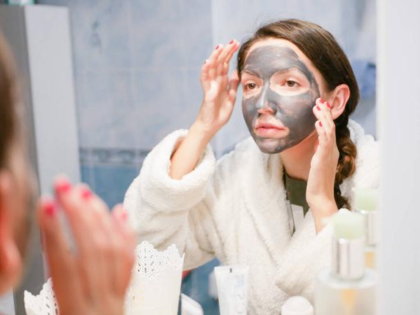 Lány és arc maszk. Egy nő szénhidrátos fekete maszkkal az arcán. A lány gondoskodik az olajos bőrről. Kozmetikai eljárások. Bőrápolás. - Fotó, kép