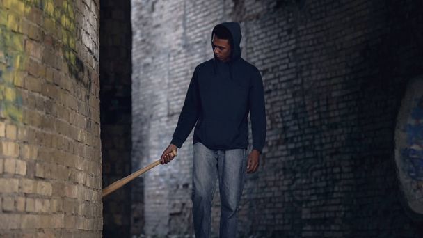 Black teenager walking abandoned city area with baseball bat, city danger - Foto, Bild