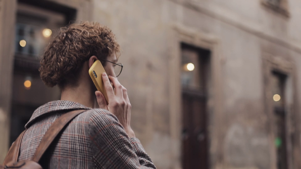 Side Back View of Young Man in Glasses with Bag Talking on the Phone під час блукання на Олд-Сіті-стріт. Комбінація, ідея студента. - Кадри, відео