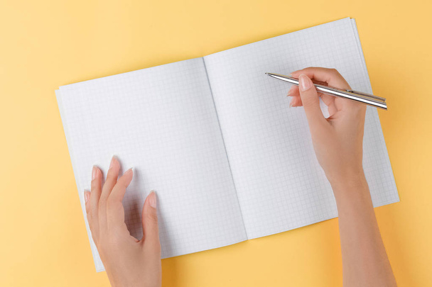 Dziewczyna pisze w otwartym notebooku widok z góry, żółte tło - Zdjęcie, obraz