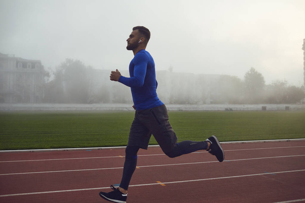 A young athlete runs on a stadium in the fog. - 写真・画像