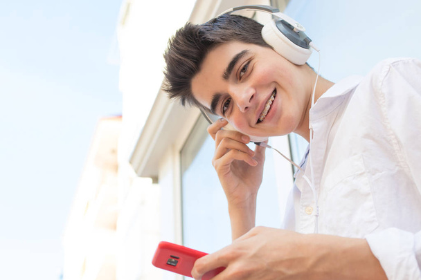 Junger Mann mit Telefon und Kopfhörer hört Musik im Freien in der Stadt - Foto, Bild
