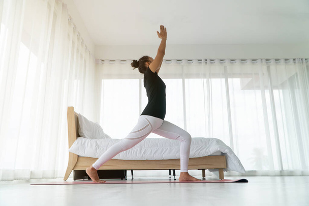 Middelbare leeftijd vrouwen doen yoga in de slaapkamer op de ochtend, Adho Mukha Svanasana pose. Concept van oefening en ontspanning in de ochtend. - Foto, afbeelding