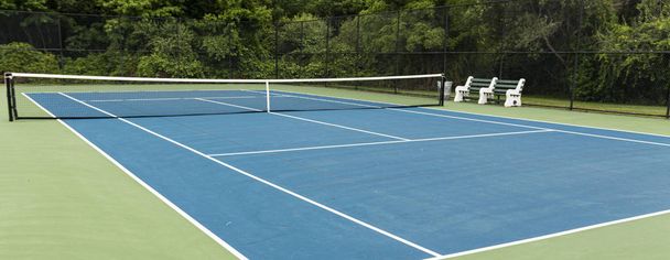 Widok na niebieski kort tenisowy z zielonym pokładzie i ławki do  - Zdjęcie, obraz