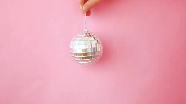 Jednoduše minimální design žena ruka drží vánoční ozdoby disco koule izolované na růžové pastelové barevné trendy pozadí. Vánoce Nový rok prosinec čas na oslavu konceptu. Kopírovat prostor - Záběry, video