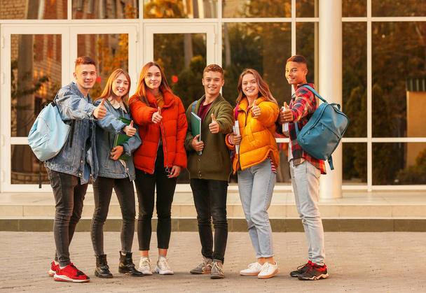 Ryhmä teini-ikäiset opiskelijat osoittavat peukalo-up lähellä yliopistoa
 - Valokuva, kuva