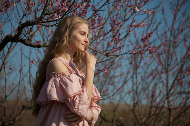 Gyönyörű szőke nő rózsaszín ruhában sétál a virágzó kertben. - Fotó, kép