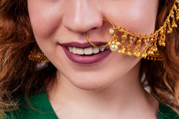 indian beautiful fashion brunette woman in green traditional sari with gold jewelry set nose ring piercing nath on white studio background bindi close-up. - Foto, immagini
