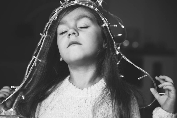 Cute little smiling girl with christmas luminous garland on her head. - Foto, imagen