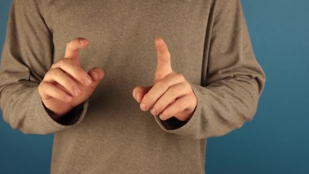de man met de grijze hoodie met lange mouwen maakt veel handgebaren tegen een blauwe achtergrond. - Video