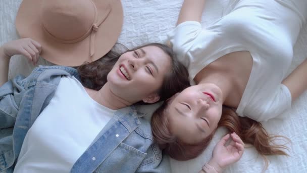 top view video of Two beautiful Asian girls who are friends are lying and chatting in a good mood on the bed. Friendship Concept - Metraje, vídeo
