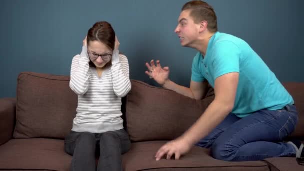 Un joven le grita a una joven. La mujer cubrió sus oídos con sus manos para no oír al hombre. Sentado en el sofá - Metraje, vídeo