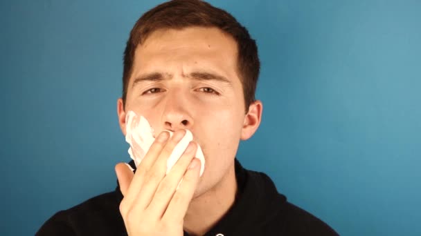 een man smeert zijn gezicht met scheerschuim op een blauwe achtergrond. - Video