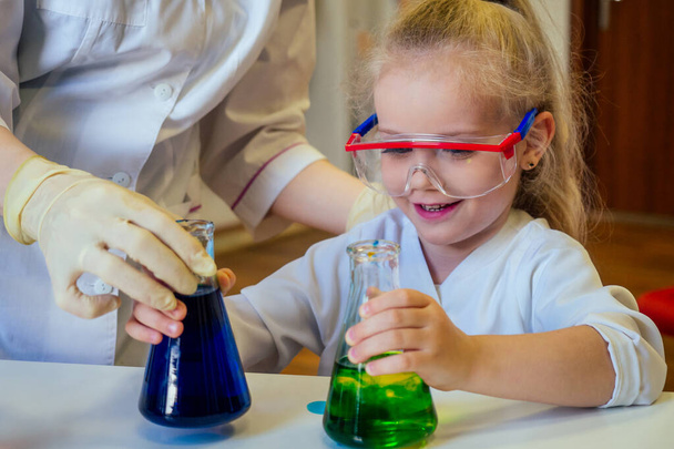 surpreendido e surpreendido inteligente loira estudante menina química em óculos e vestido médico branco fazendo experimentos científicos química, misturando diferentes soluções químicas em sala de aula de laboratório
 - Foto, Imagem