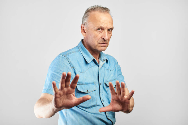 Caucasian senior citizen put his hands forward, refuses the offer, does not want to participate in dubious transactions isolated in white studio - Фото, зображення