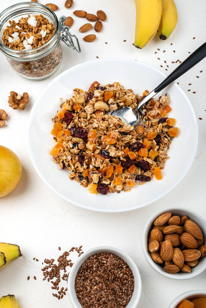 Granola muesli breakfast with with milk, dried apricots, cranberries, almonds and flax seeds in bowl on a white background. Healthy cereal breakfast. - Photo, Image