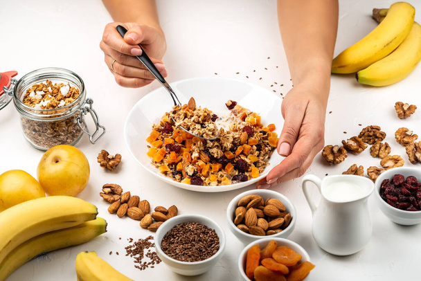 Vrouw die ontbijtschaal van muesli granola eet met melk, gedroogde abrikozen, cranberries, amandelen en lijnzaad. Vrouwelijke handen houden gezonde natuurlijke detox voedsel. - Foto, afbeelding
