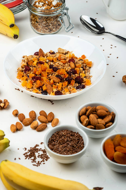 Healthy breakfast. Granola muesli with milk, dried apricots, cranberries, almonds and flax seeds in a white bowl on white background. Clean eating, diet, detox, vegetarian food. - Fotó, kép