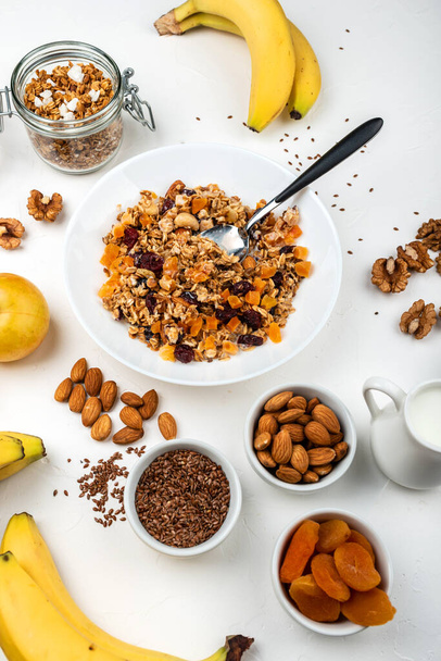 Healthy breakfast. Granola muesli with milk, dried apricots, cranberries, almonds and flax seeds in a white bowl on white background. Clean eating, diet, detox, vegetarian food. - Foto, afbeelding