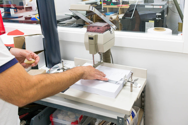 werknemer manipuleren papier ponsen machine in de werkplaats - Foto, afbeelding