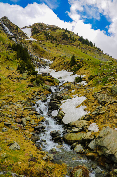 Bergstroom stroomt langs de berghelling, sneeuw. Natuur achtergrond in het voorjaar of de zomer. Selectieve focus. - Foto, afbeelding