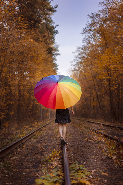 Een jong meisje met een veelkleurige paraplu loopt langs de tram. Wandeling door het herfstbos. - Foto, afbeelding