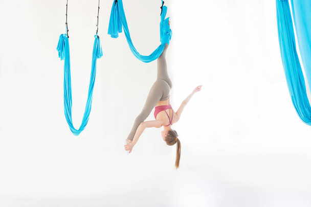 Hermosa joven sonriendo a la práctica de aero fly yoga en estudio blanco sobre hamacas azules. Concepto de meditación de estiramiento
, - Foto, Imagen