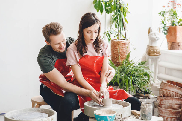 Young romantic couple working on potter wheel and sculpting clay pot. Concept ceramics - 写真・画像