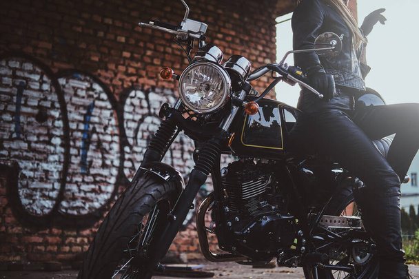 Mulher motociclista em preto com sua moto ao lado da parede de graffity
 - Foto, Imagem