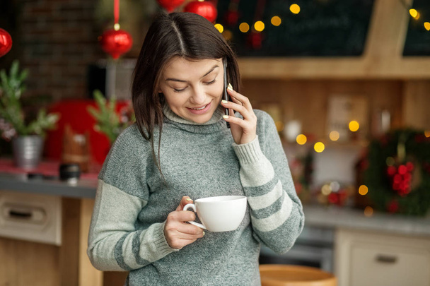 Красивая женщина говорит по мобильному телефону. Девушка пьёт чай. Зимняя концепция, образ жизни, веселье и Новый год. Концепция зимы, образа жизни, Рождества и Нового года
. - Фото, изображение