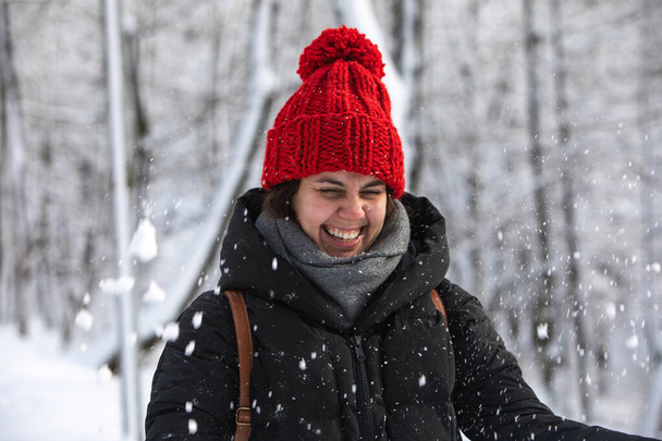молода досить усміхнена жінка в зимовому пальто з червоним капелюхом в міському лісовому парку
 - Фото, зображення
