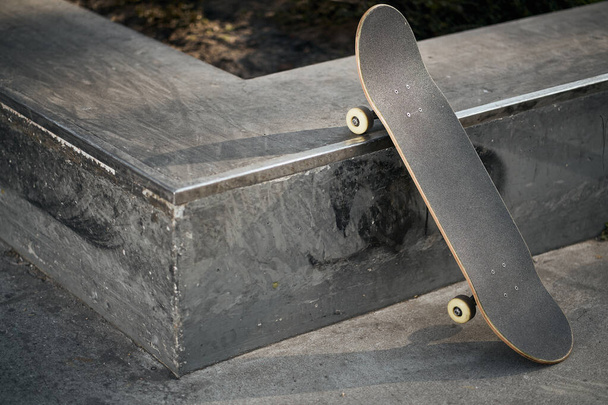 Uitzicht op zwart skateboard in betonnen skatepark op warme dag - Foto, afbeelding