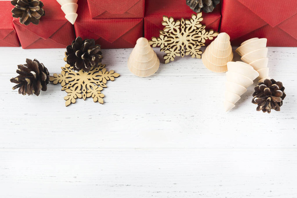 Red gifts with eco Christmas decoration. New year composition with wooden toys and natural pine cones. Copy space - Foto, Bild