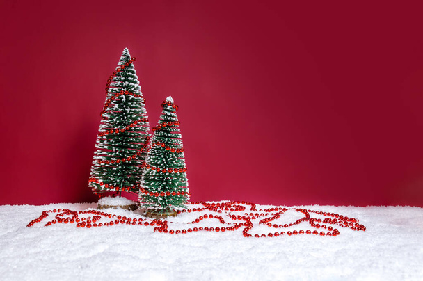 コピースペース付きの赤い背景にビーズの文字列で飾られたモミの木とクリスマスの背景 - 写真・画像