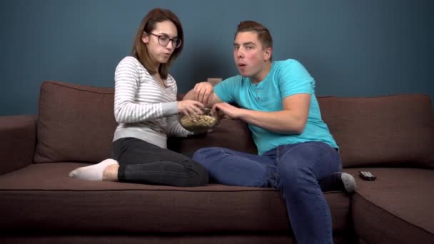 Young man and woman watching TV and eating popcorn. Couple fighting for a plate with popcorn. Watch TV carefully - Footage, Video