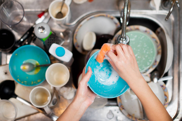 girl washes a dirty plate on the background of the sink with dirty dishes - Fotó, kép